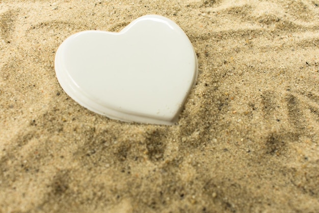 Coeur en porcelaine blanche sur le sable de la plage