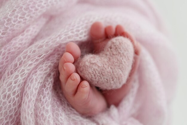 Coeur rose tricoté dans les jambes d'un bébé Pieds doux d'un nouveau-né dans une couverture en laine rose Gros plan des orteils talons et pieds d'un nouveau-né Macro photographie le petit pied d'un nouveau-né