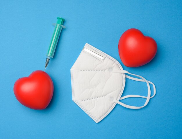 Coeur Rouge Et Une Aiguille Coincée D'une Seringue En Plastique Dedans, Masque Blanc Sur Fond Bleu