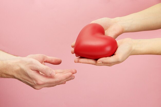 Coeur rouge dans les mains de la femme et de l'homme, sur fond rose