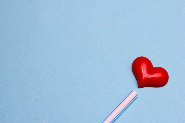 Un coeur rouge sur fond bleu près d'un tube à cocktail en plastique. Concept de la Saint-Valentin. L'idée de l'amour. Copiez l'espace.
