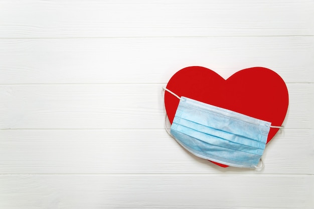 Coeur rouge avec masque de protection jetable bleu sur bois texturé blanc