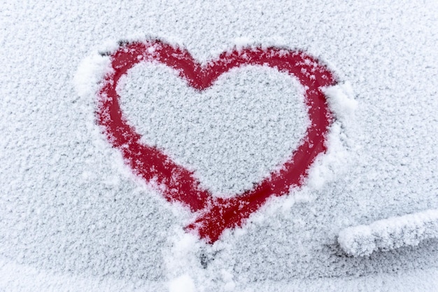 Coeur rouge de neige sur la fenêtre de la voiture avec espace de copie Signe de coeur dans des flocons de neige frais Symbole de forme de coeur dessiné sur le verre de voiture enneigé Concept d'amour Saint Valentin Déclaration d'amour