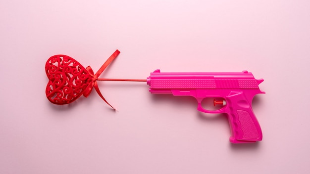 Coeur rouge avec pistolet rose sur fond pastel rose