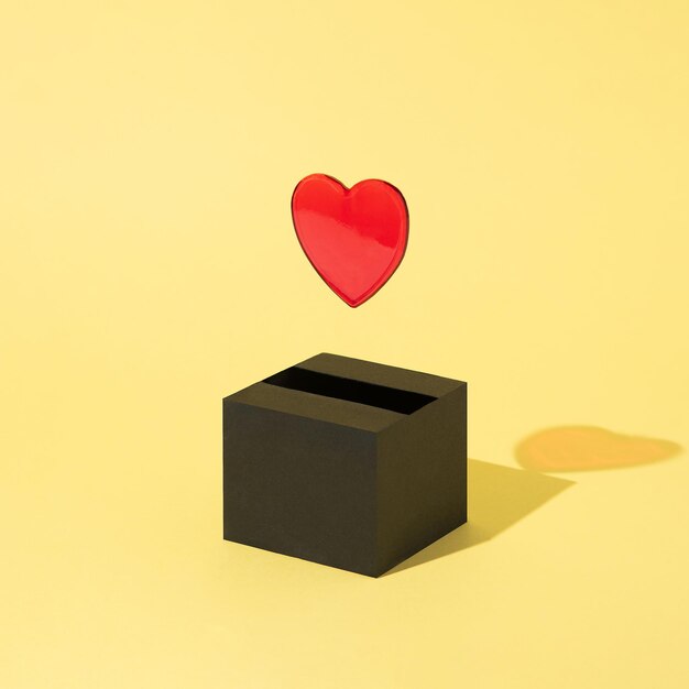 Le coeur rouge sort d'une boîte noire et flotte sur un fond jaune Résumé de la Saint-Valentin