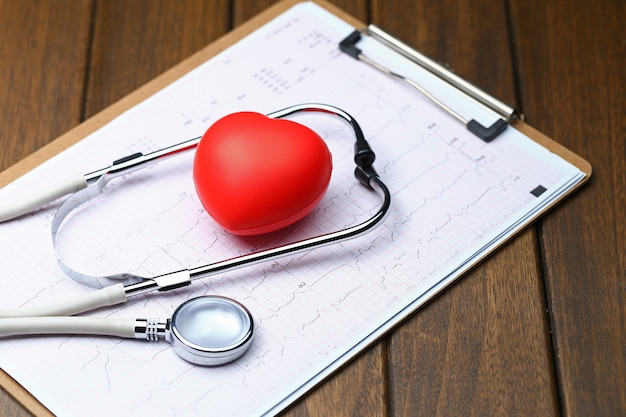 Cœur rouge avec stéthoscope et électrocardiogramme sur fond de bois