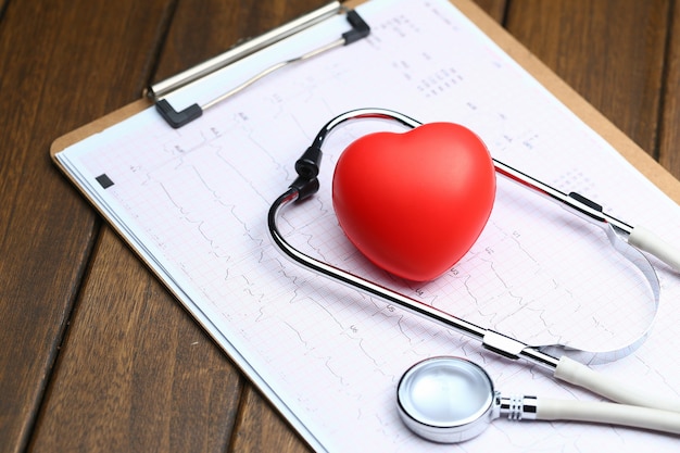 Cœur rouge avec stéthoscope et électrocardiogramme sur fond de bois