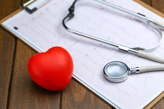 Cœur rouge avec stéthoscope et électrocardiogramme sur fond de bois