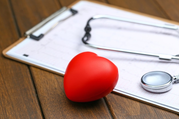 Coeur rouge avec stéthoscope et électrocardiogramme sur fond de bois