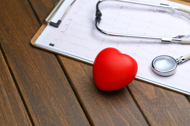 Cœur rouge avec stéthoscope et électrocardiogramme sur fond de bois