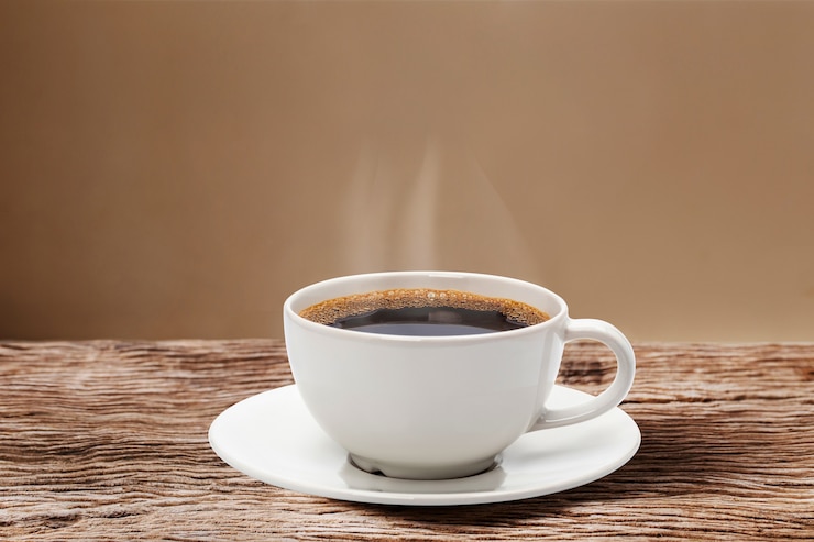 Coeur de vapeur planant au-dessus d'une tasse de café rouge sur une table en bois avec mur crème