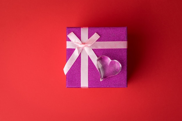Coeur en verre en haut d'un coffret cadeau sur fond rouge. Une déclaration d'amour.