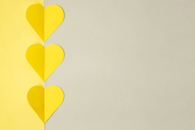 Coeurs jaunes découpés dans du papier de couleur sur fond gris, vue de dessus, couleurs 2021. Concept de Saint Valentin aux couleurs tendance.