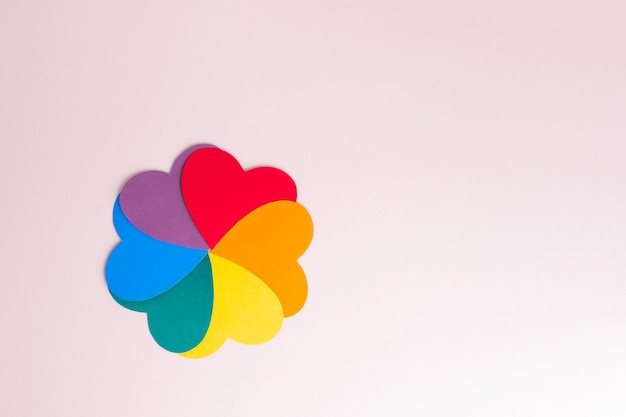 Coeurs en papier multicolores formant une forme de fleur avec des pétales d'arc-en-ciel sur un espace de copie de fond rose