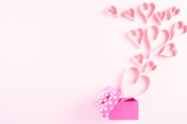 Coeurs en papier rose éclaboussent de boîte-cadeau sur fond de papier pastel rose