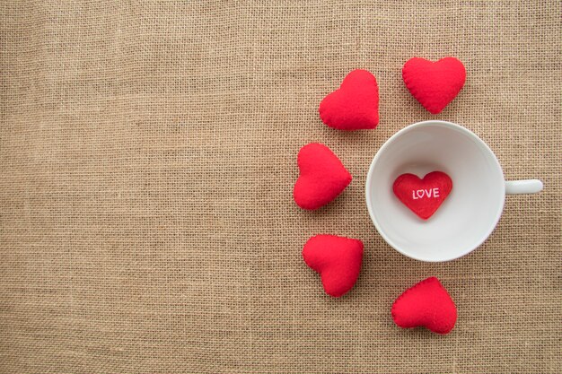 Coeurs rouges autour de la tasse et dans la tasse de café sur fond de texture de sac