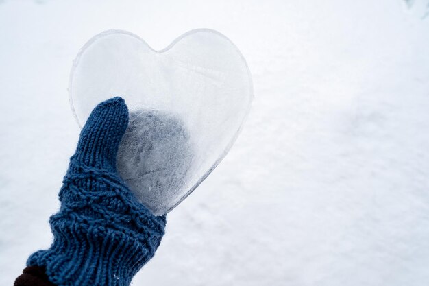 Photo les coeurs, symbole de l'amour fait de glace, sont tenus par une main dans des mitaines tricotées bleu chaud