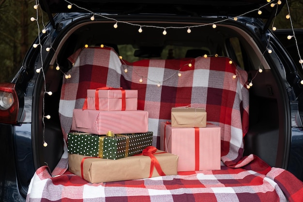 Coffre de voiture rempli de coffrets cadeaux, de cadeaux et de guirlandes pour les vacances de Noël. forêt en plein air