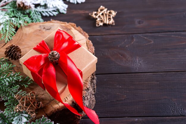 Coffret brun avec un arc rouge, décoration de Noël sur une planche à découper en bois sur en bois foncé, vue de dessus