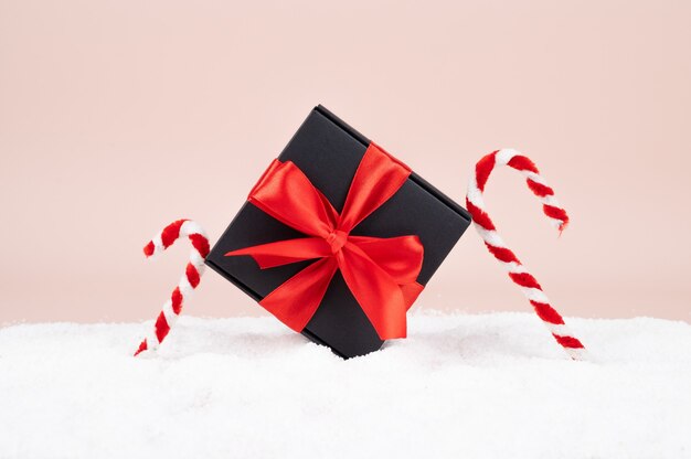 Coffret cadeau avec arc rouge et cannes de bonbon dans la neige sur une surface rose. Contexte festif. photo de haute qualité