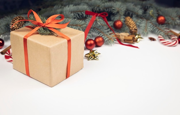 Coffret cadeau artisanal avec ruban rouge sur fond de cônes de branches d'arbres de Noël et de boules de Noël sur fond blanc Concept de voeux de vacances d'hiver