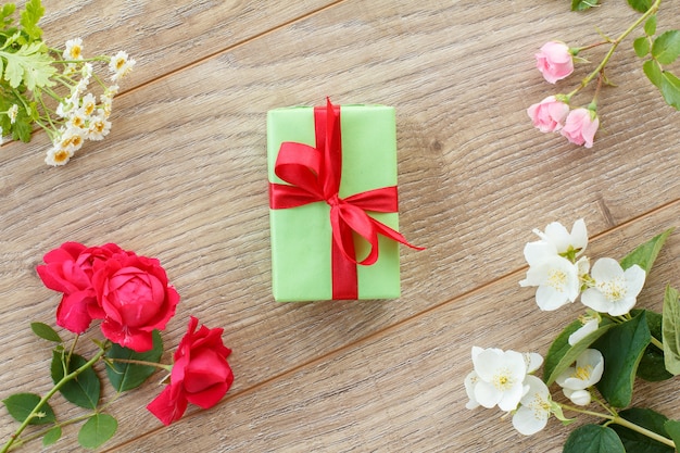 Coffret cadeau avec et belles roses, fleurs de jasmin et de camomille sur le fond en bois. Concept de donner un cadeau en vacances. Vue de dessus.