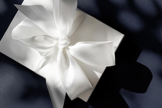 Coffret cadeau blanc de vacances de luxe avec ruban de soie et noeud sur fond noir mariage de luxe ou cadeau d'anniversaire