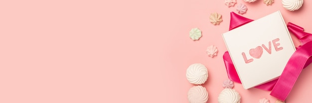 Coffret cadeau et bonbons, guimauves et meringues sur une surface rose pastel