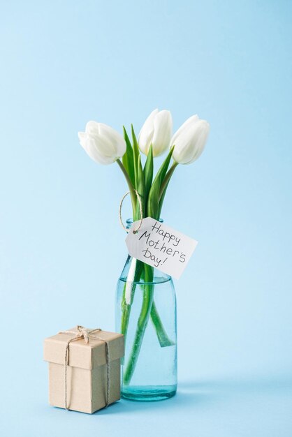 Coffret cadeau et bouquet de tulipes blanches avec étiquette de voeux bonne fête des mères sur fond bleu