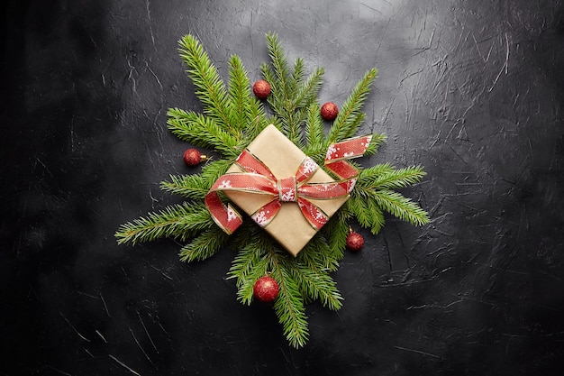 Coffret cadeau avec branche d'arbre de Noël verte et boules rouges sur fond noir vue de dessus