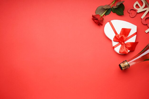 Coffret cadeau avec champagne pour la Saint-Valentin et roses sur fond rouge, espace pour le texte, mise à plat.