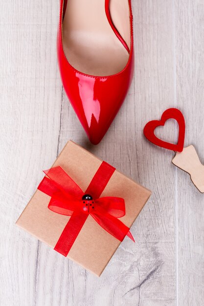 Coffret cadeau et chaussure rouge. Petit coeur sur fond en bois. Félicitez votre petite amie. Cadeau pour une dame élégante.