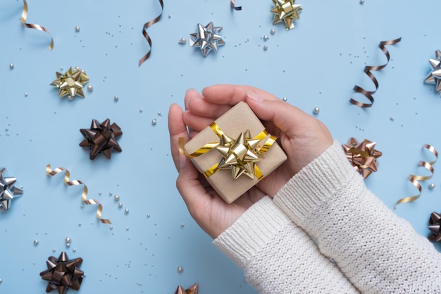 Coffret cadeau dans des mains féminines sur fond festif lumineux avec des arcs et des perles vue de dessus