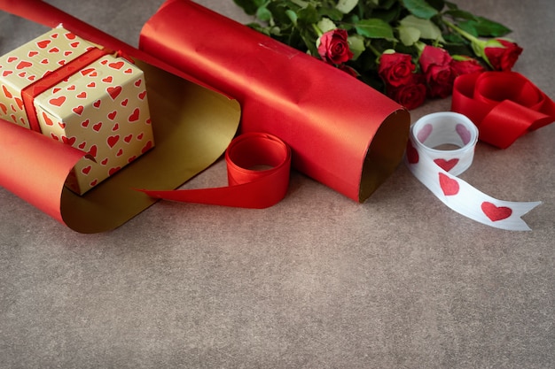 Coffret cadeau emballé dans du papier rouge, des roses et des matériaux d'emballage sur du brun