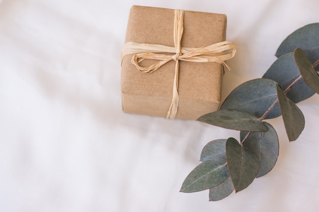 Coffret cadeau enveloppé dans du papier Kraft marron avec une branche d'eucalyptus sur un tissu en lin blanc