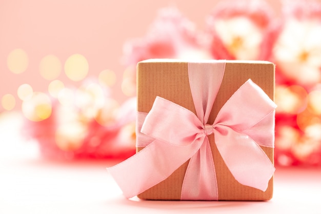 Coffret cadeau enveloppé de papier kraft et noeud rose sur fond de fleurs roses.