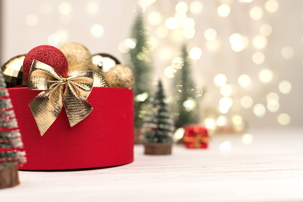 Coffret cadeau de Noël rouge avec un arc d'or sur fond de bokeh, arbres de Noël et jouets.