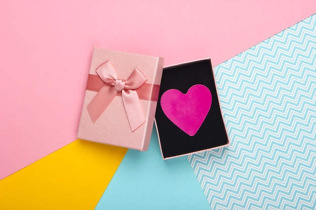 Coffret cadeau avec noeud et coeur décoratif sur fond coloré. La saint Valentin. Tendance couleur pastel. Vue de dessus