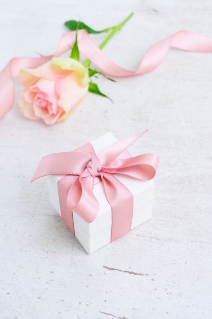 Coffret cadeau avec un noeud en satin rose et rose sur fond de bois blanc