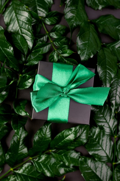 Coffret cadeau noir de luxe avec ruban vert sur fond sombre avec des feuilles sur les côtés, à plat, concept nature.