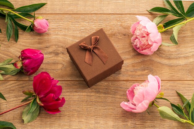 Coffret cadeau noyer sur des planches en bois décorées de fleurs de pivoine rouges et roses. Vue de dessus.