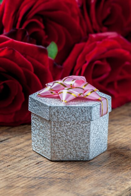 Coffret cadeau avec ruban rose et roses rouges derrière