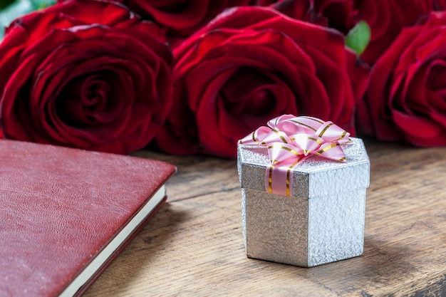 Photo coffret cadeau avec ruban rose et roses rouges derrière