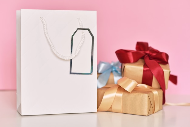 Photo coffret cadeau avec sac shopping en ruban et papier sur fond rose