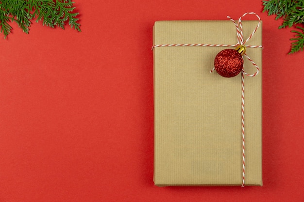 Coffret cadeau vintage enveloppé de Noël avec ruban, décoration et branches de thuya sur fond rouge. Maquette d'appartement de vacances. Vue de dessus. Espace de copie.