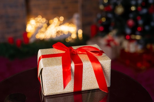 Coffret doré attaché avec un ruban rouge avec un arc sur le fond d'un arbre de Noël