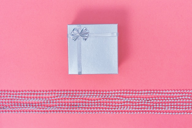 Coffret fermé argent brillant sur papier couleur rose. Composition de style minimal.