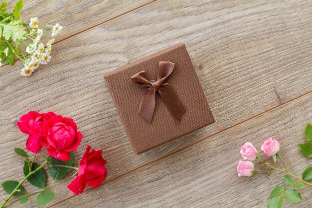 Coffret marron avec de belles roses et fleurs de camomille sur le fond en bois. Concept de donner un cadeau en vacances. Vue de dessus.