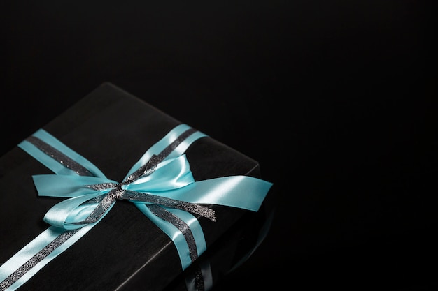 Coffret noir avec un noeud turquoise sur une surface noire. Carte. Espace pour le texte.