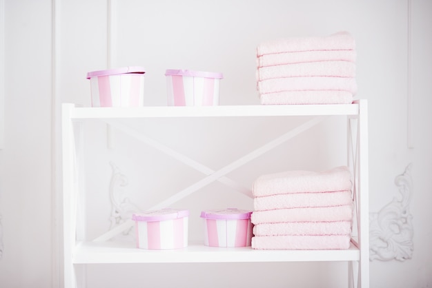 Coffret pour accessoires et serviettes roses propres sur l'étagère blanche. Tablette avec accessoires de femme dans la salle de bain.